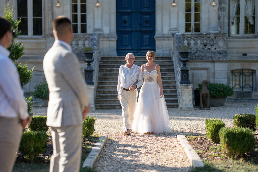 Bride being walked down the aisle in front of a grand house.