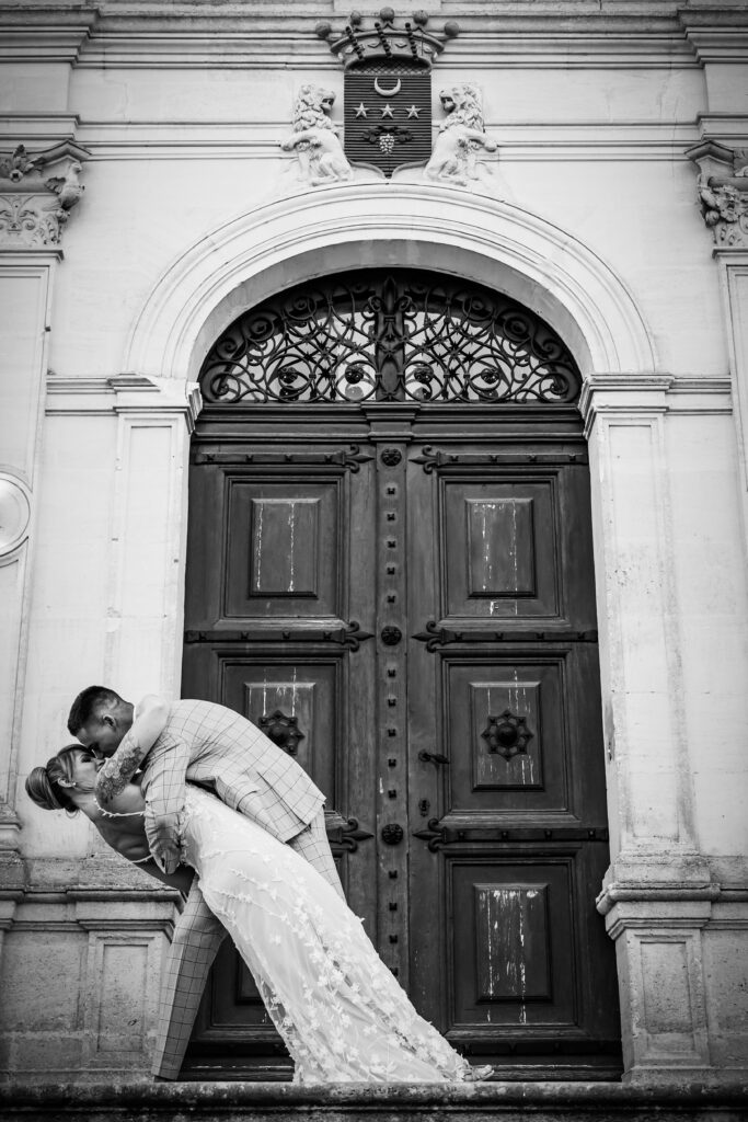Black and white photo of the groom dipping the bride in front of an ornate castle doorway.