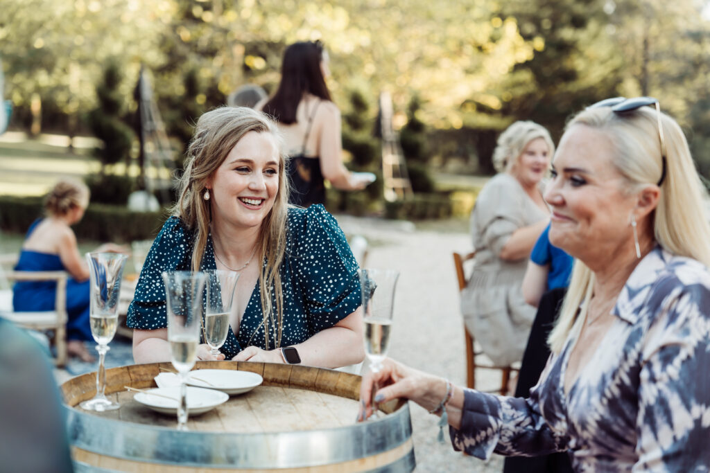 Wedding guests chatting and drinking wine around barrel tables.