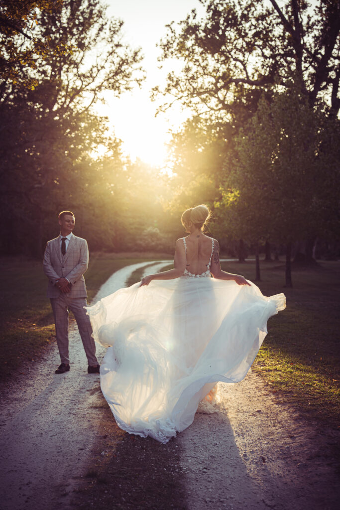 Bride and groom walking along a sunlit woodland path at golden hour, with the bride lifting her dress as they walk.