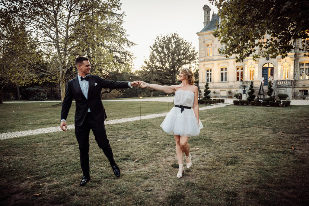 Bride and groom standing with outstretched arms in the front garden of a grand country house.