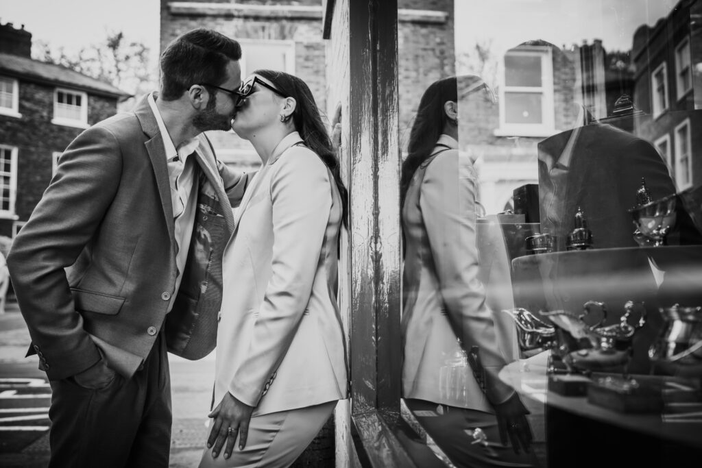 Black and white photo of the wedding couple kissing beside a window, with their reflection mirrored in the glass.