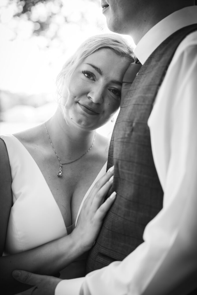 Black and white photo of the wedding couple, with the bride resting her head on the groom's chest.