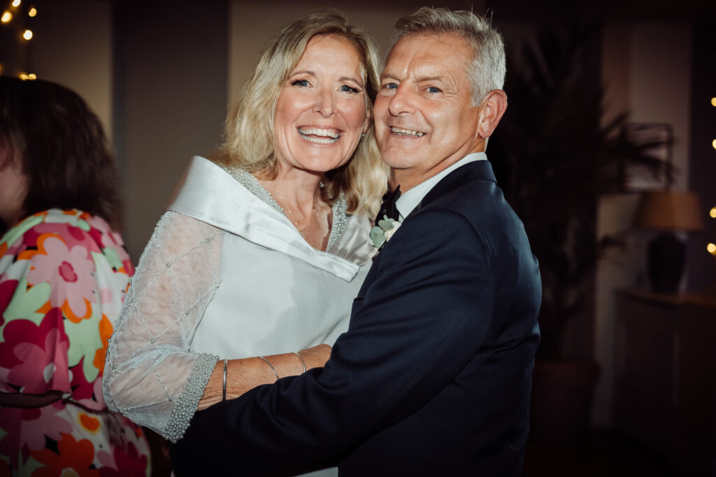 A mature bride and groom embrace and smile at the camera.