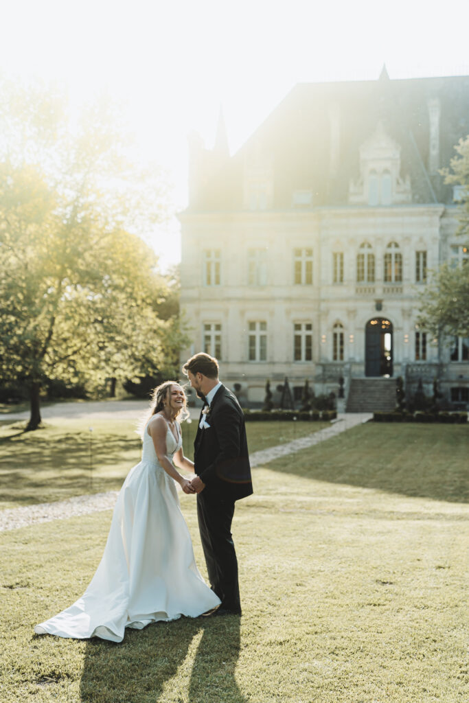 Couple holding hands in front of Chateau De La Valouze, France, during a destination wedding photography session.