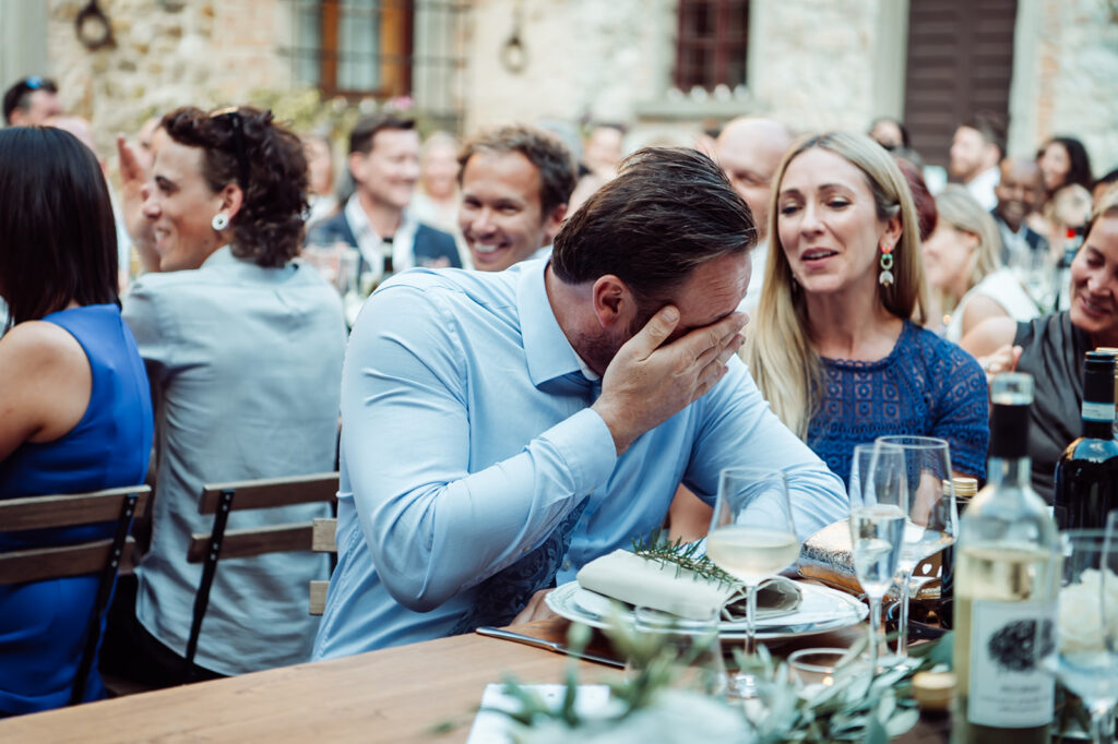 Wedding guest wiping away tears while seated among other guests at long tables during a reception.