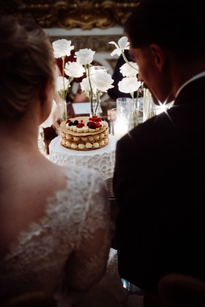 View of a wedding cake seen over the shoulders of a Bride and Groom