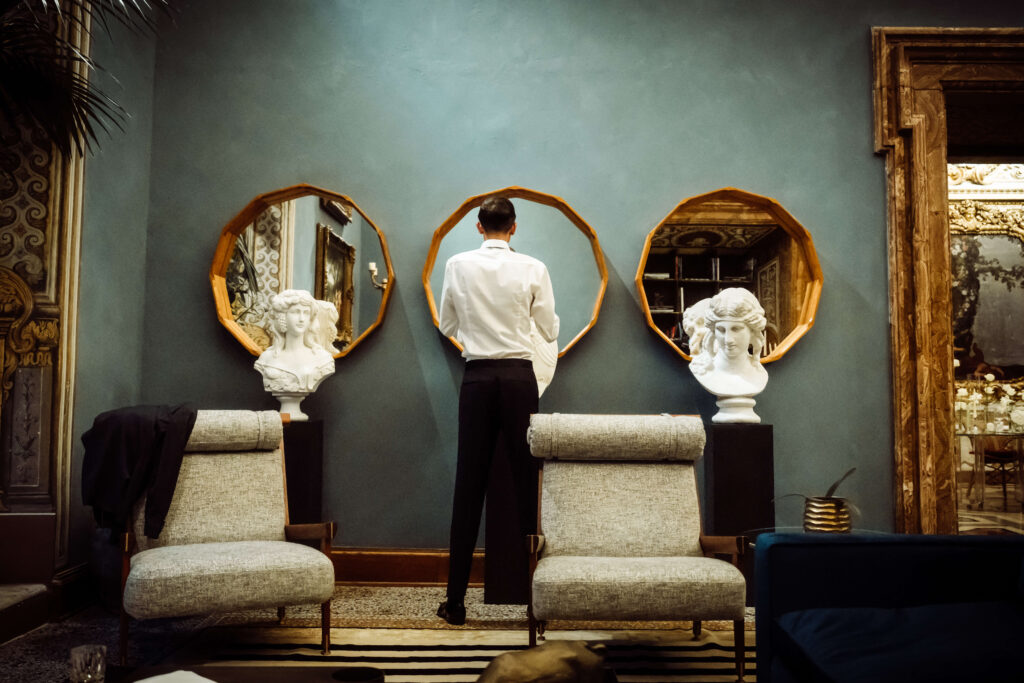 Back view of a Groom standing in front of three circular mirrors.