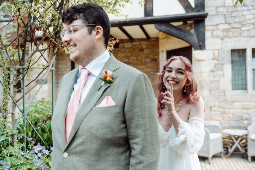 Bride holding a finger to her lips in a playful shushing gesture before the first look.