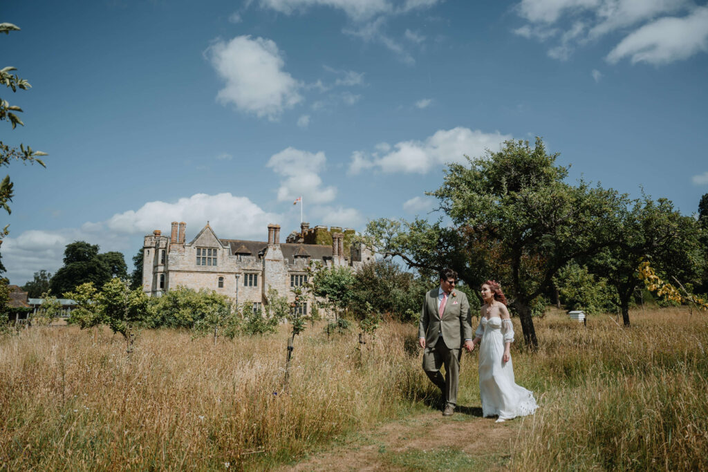 Wedding couple walking through a field with a historic building in the background.