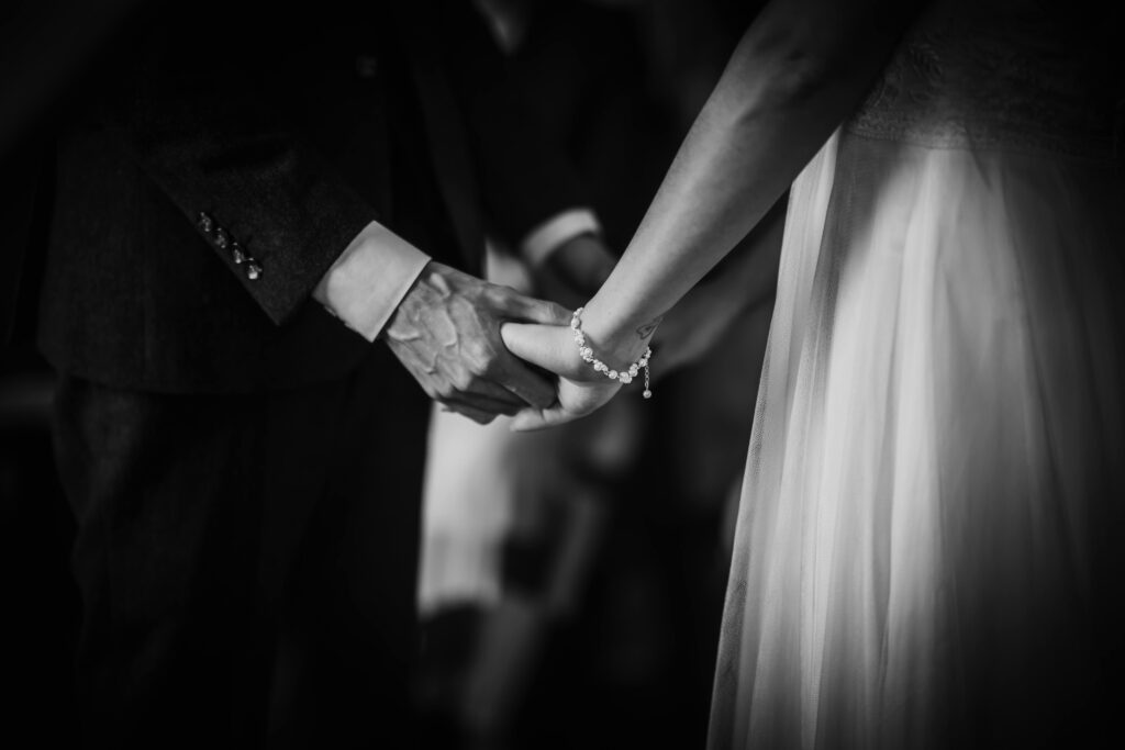 Black and white photo of the bride and groom holding hands during the wedding ceremony.