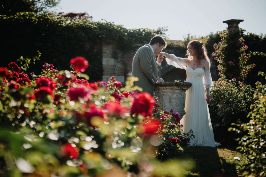 Groom kissing the bride’s hand in the gardens of Hever Castle.