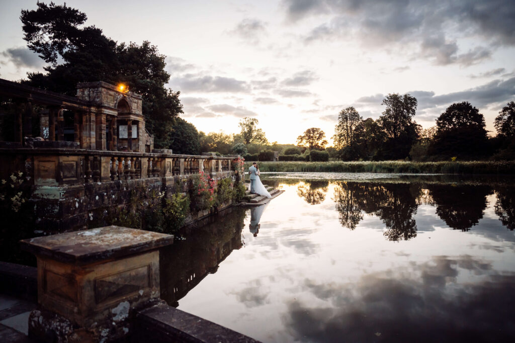 Wide shot of the Hever Castle Loggia and lake, with the wedding couple embracing on the steps.