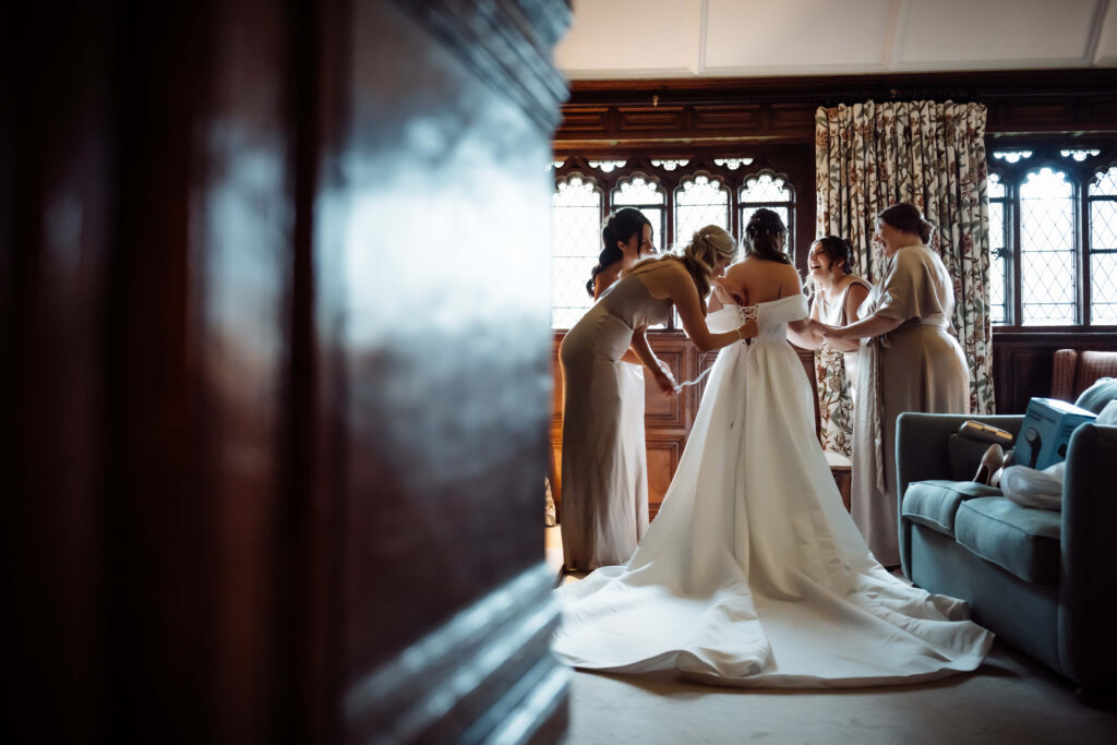 Bridesmaids helping the bride adjust her wedding dress in a room at Hever Castle.