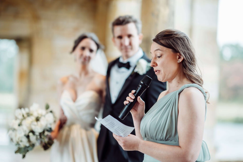 Bridesmaid giving a speech with a microphone in front of the wedding couple.