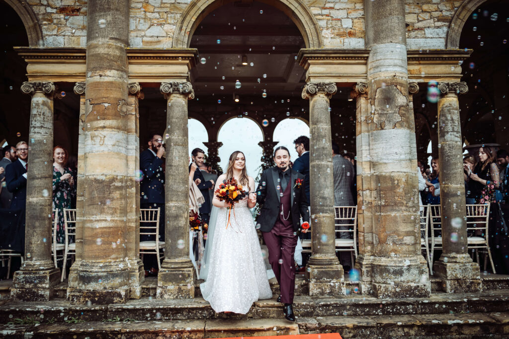 Wedding couple walking out of their ceremony surrounded by bubbles.