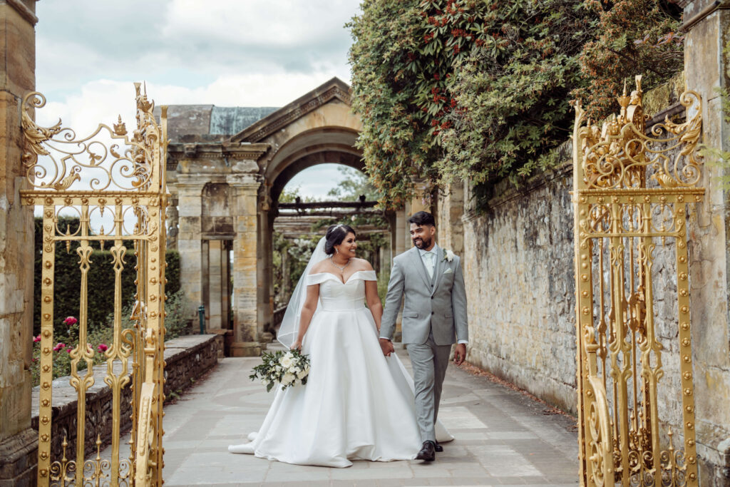 Wedding couple holding hands walking through the Hever Castle grounds.