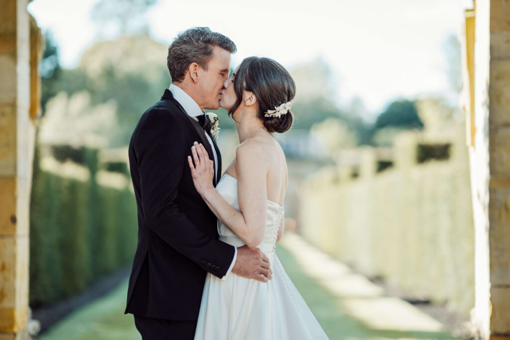 Wedding couple kissing with the gardens of Hever Castle blurred in the background.