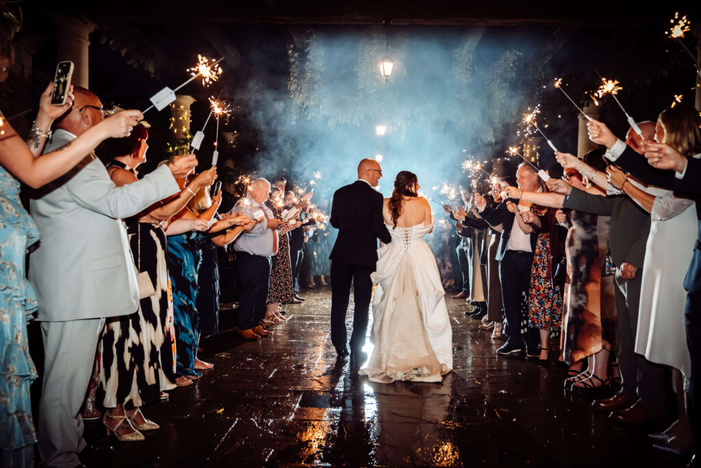 Bride and groom walking through a crowd of wedding guests holding sparklers.
