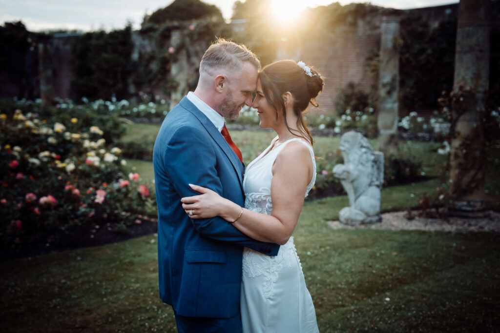 Bride and groom embracing with their foreheads touching in the gardens of Hever Castle