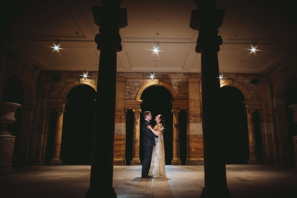 Wedding couple embracing beneath an archway illuminated by warm light.