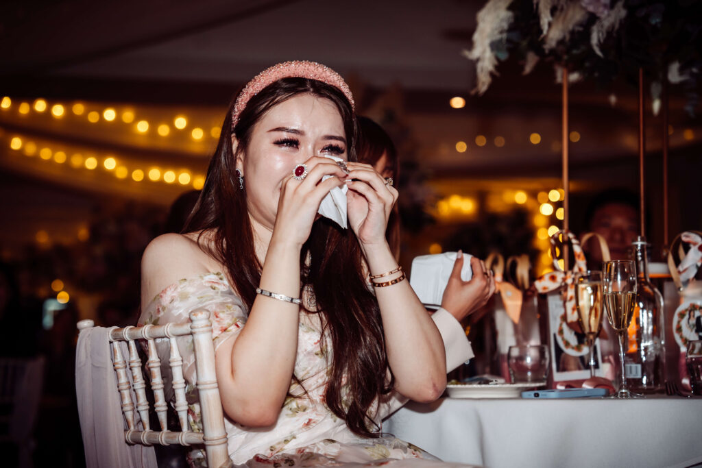 Wedding guest wiping away tears with a tissue while seated at a reception table.