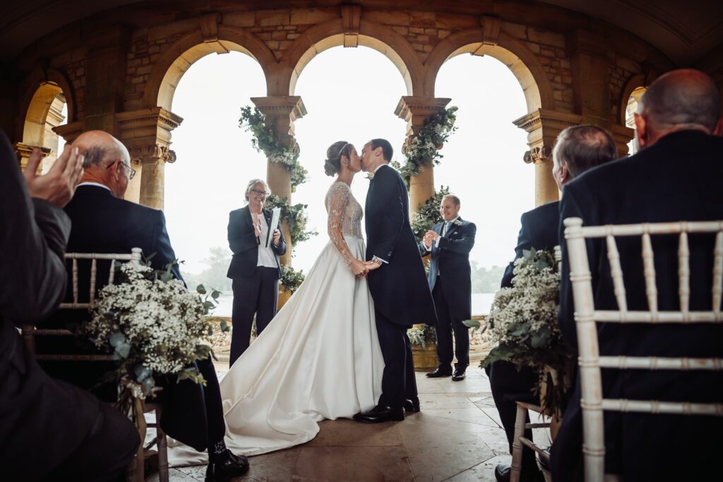 Wedding couple kissing at the ceremony while guests applaud.