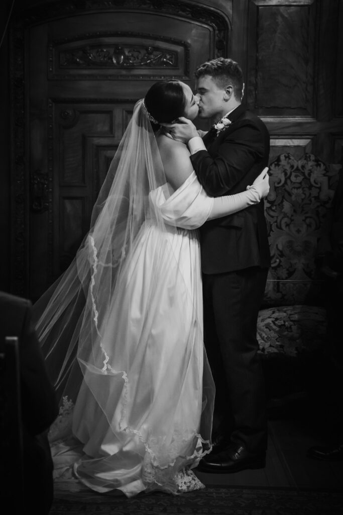 Black and white photo of the wedding couple kissing at their ceremony.