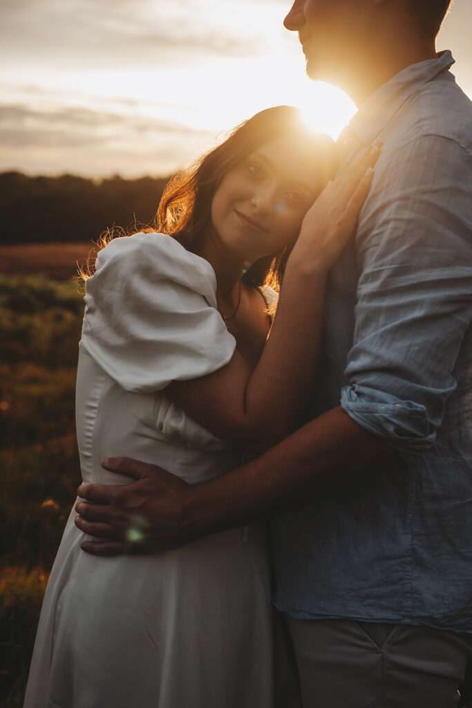Couple embracing with the woman resting her head on the man's chest, with sunset in the background.
