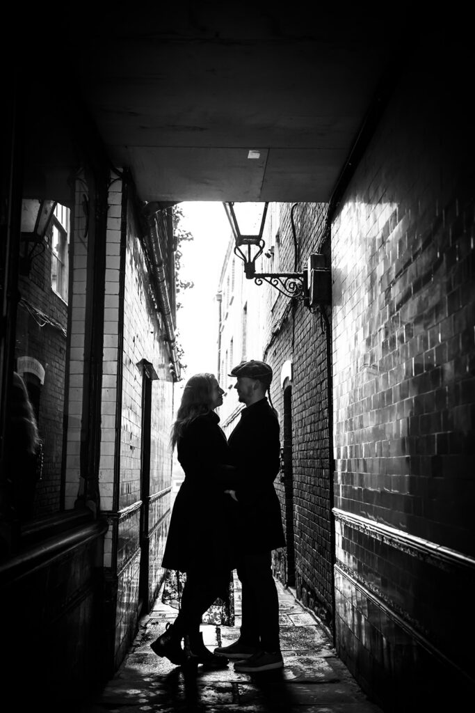 Black and white photo of a couple facing each other in an alleyway.