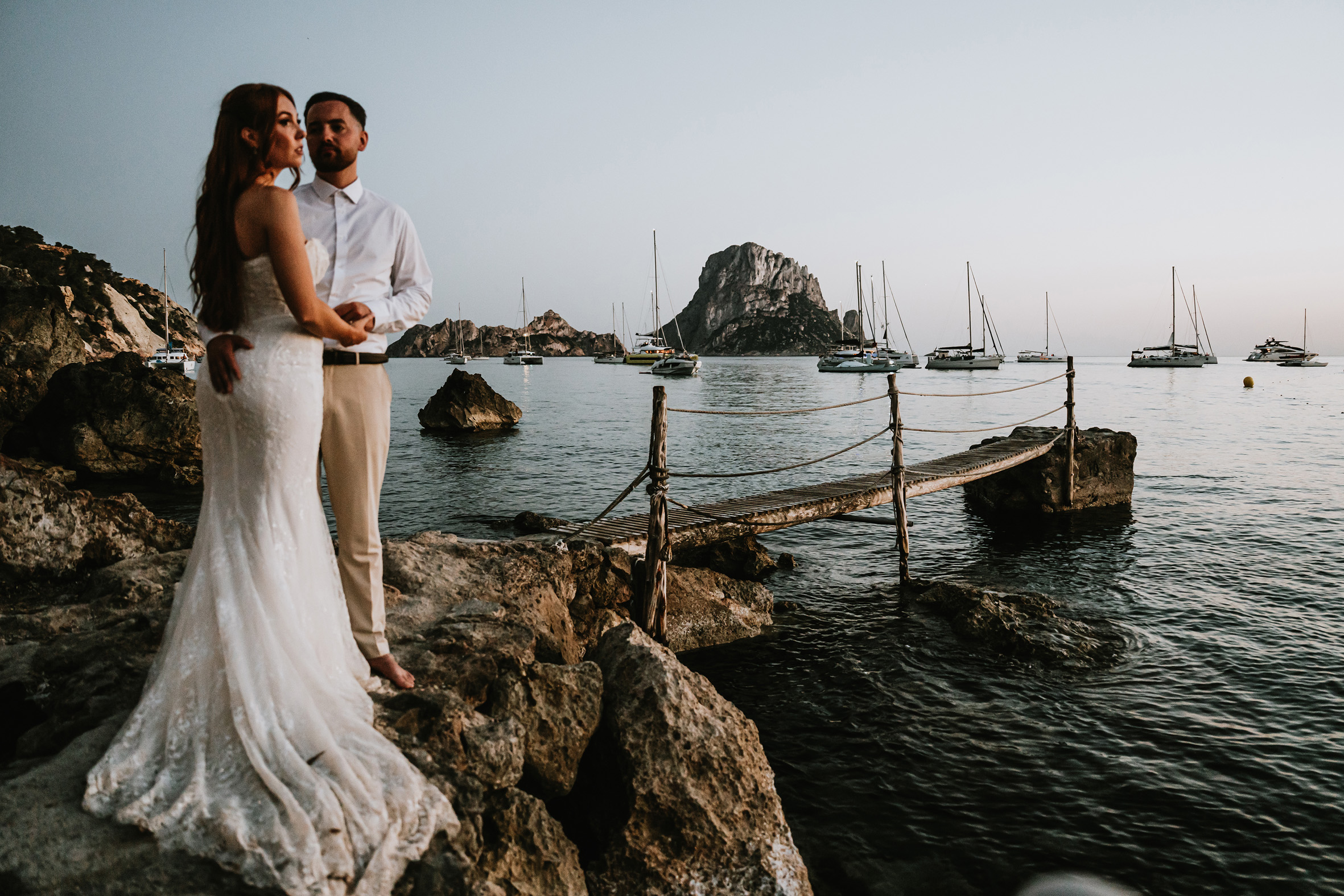 A wedding couple standing next to the water of a harbour.