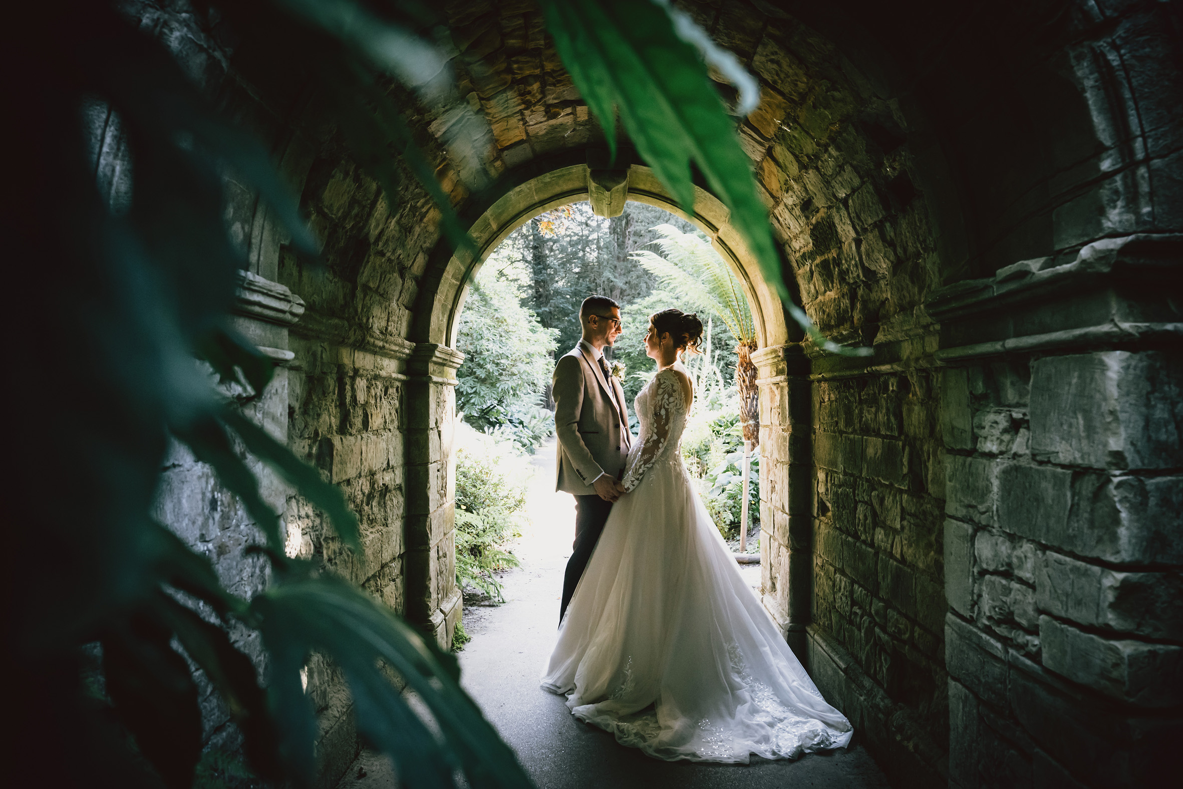 Wedding couple facing each other under a stone archway.