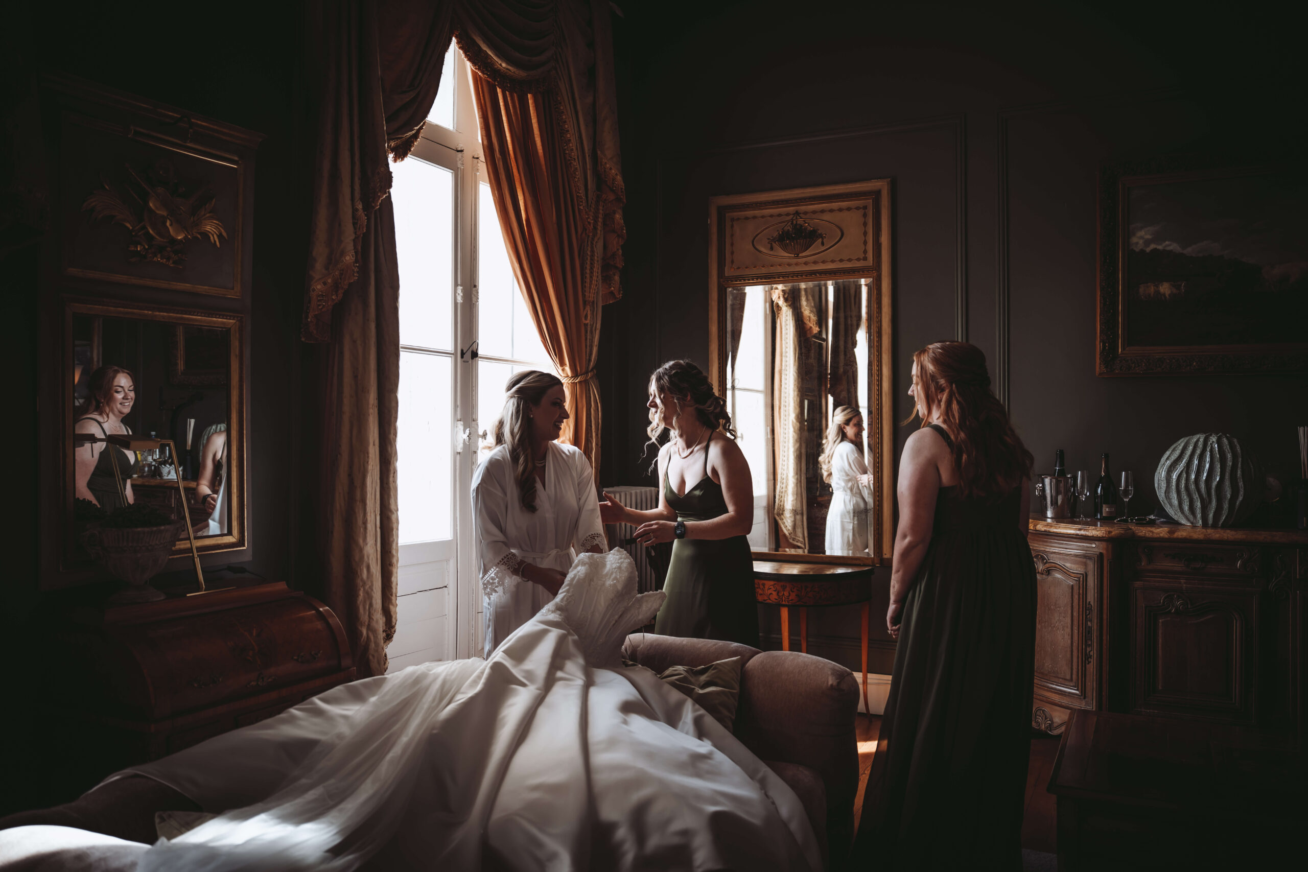 Bride getting ready with two bridesmaids in a chateau bedroom.