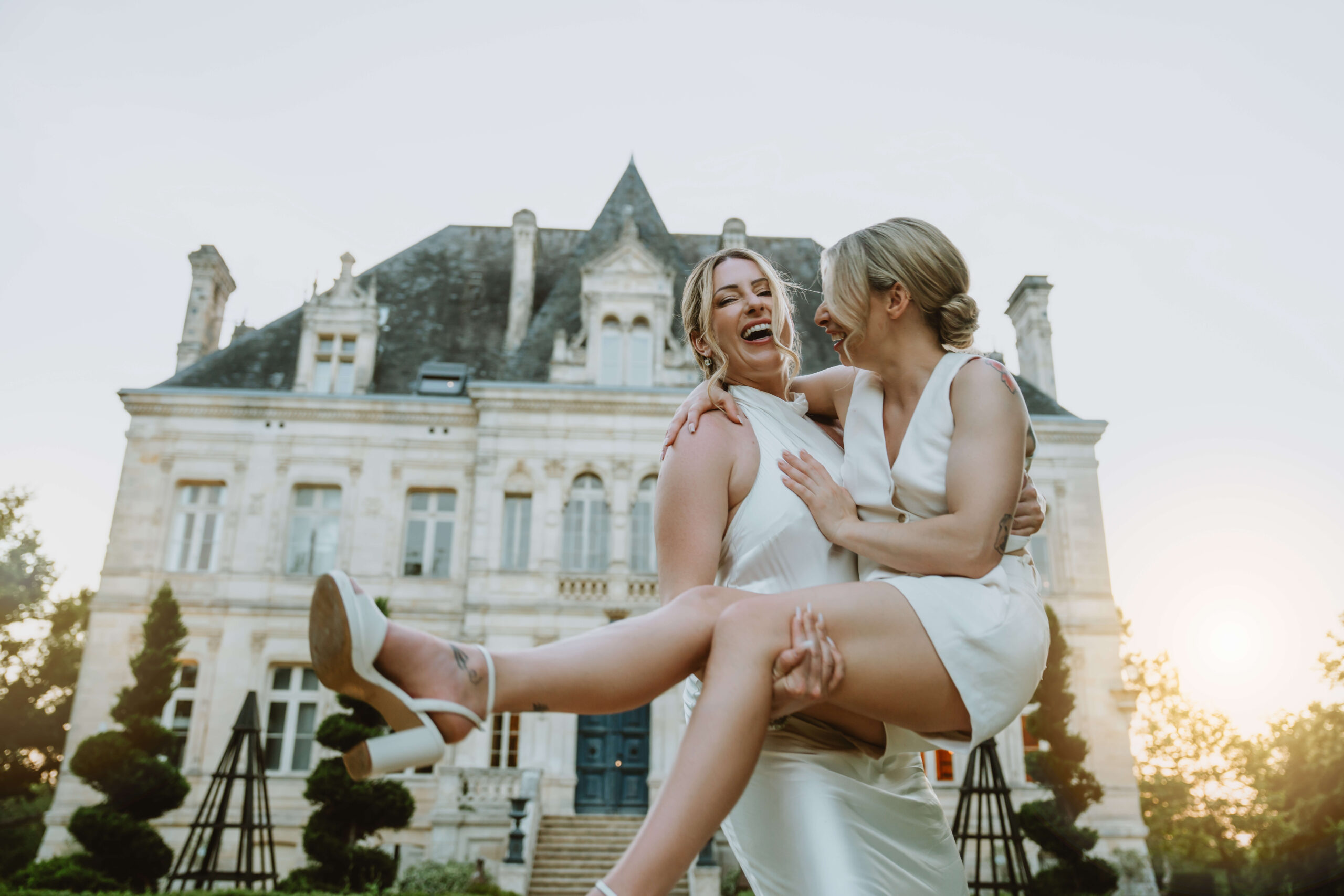One bride lifting another bride in her arms in front of French chalet