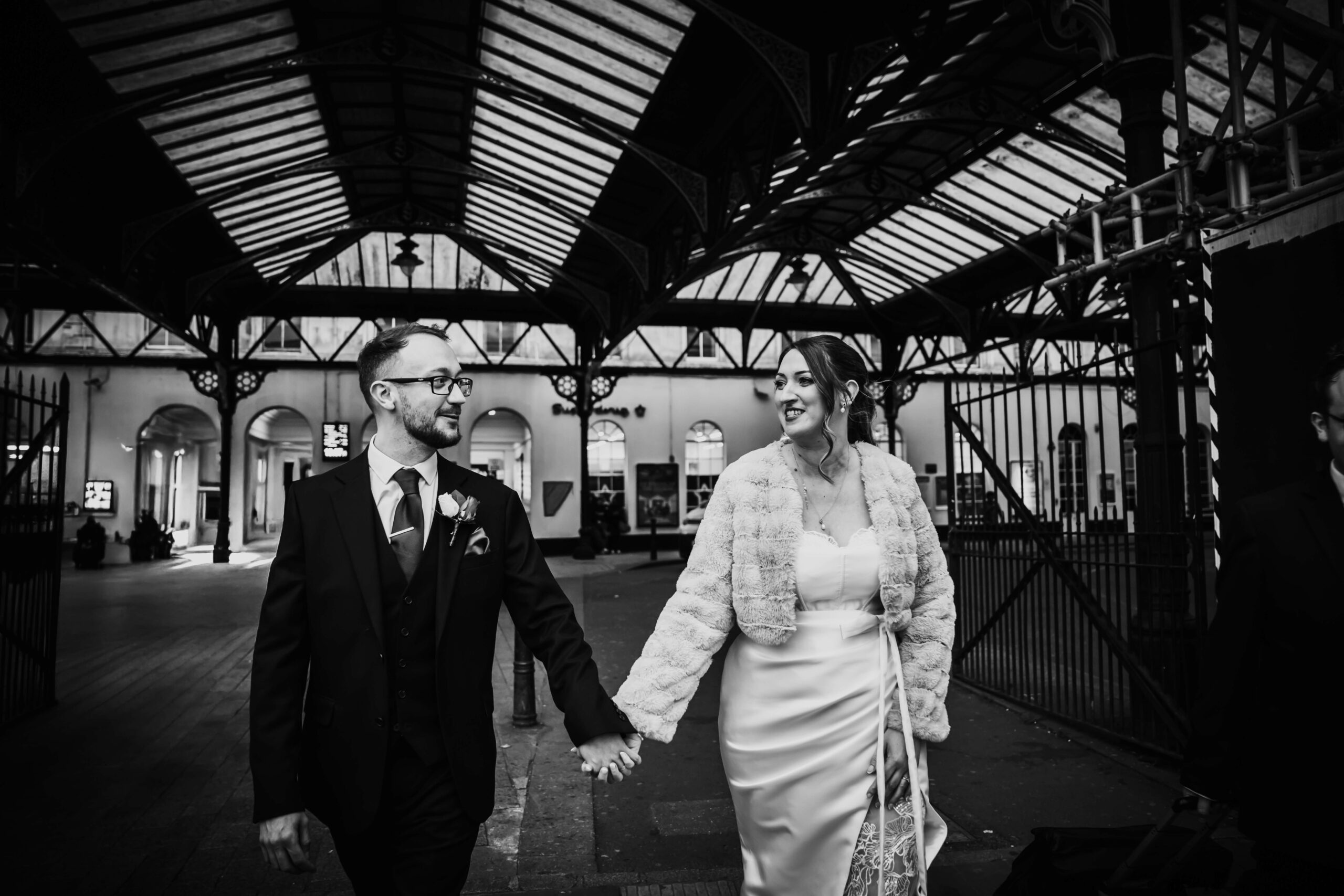 Wedding couple holding hands, walking through a train station.