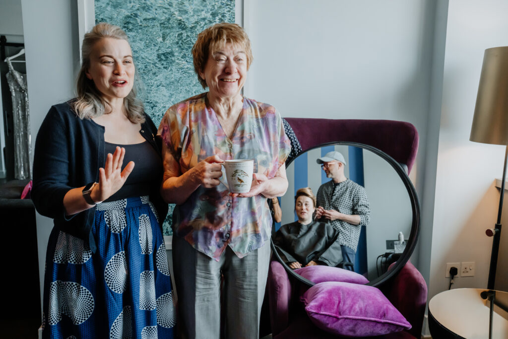 Two women smiling while watching the bride get her hair done.