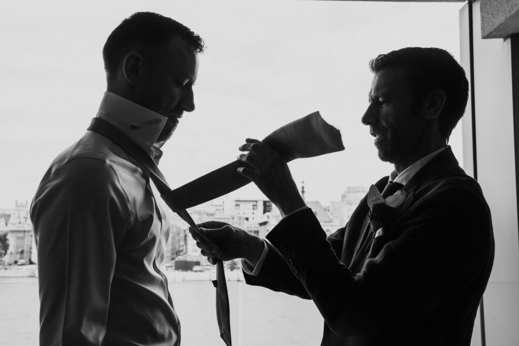 Black and white photo of groom getting help with his tie. 