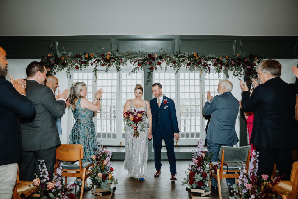 Bride and groom walking back up the aisle as guests applaud during their Swan London wedding ceremony. Captured by a UK luxury wedding photographer