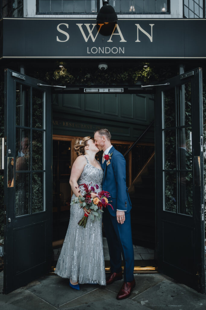Bride and groom kissing outside The Swan London entrance, captured by a UK wedding photographer The Swan London, full-body romantic moment.
