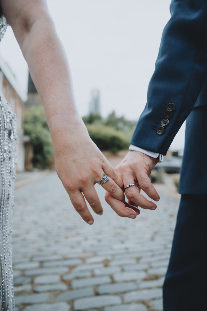 close-up of couple holding hands with wedding rings along the London Thames during a wedding photography session. Captured by a UK luxury wedding photographer