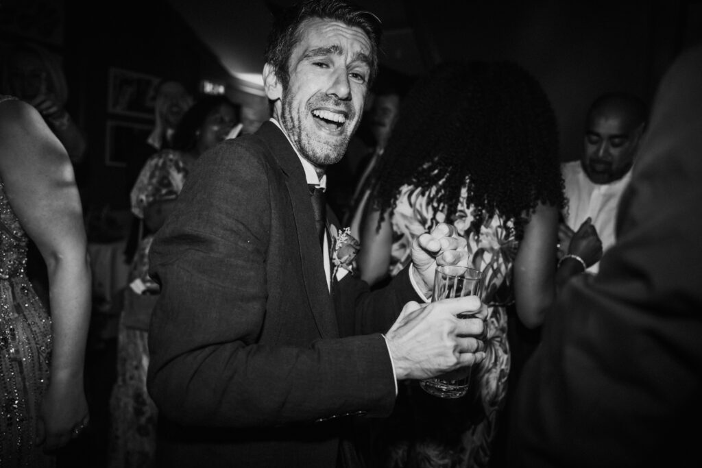black and white candid photo of a man dancing and singing at a wedding celebration in SWAN London. 
