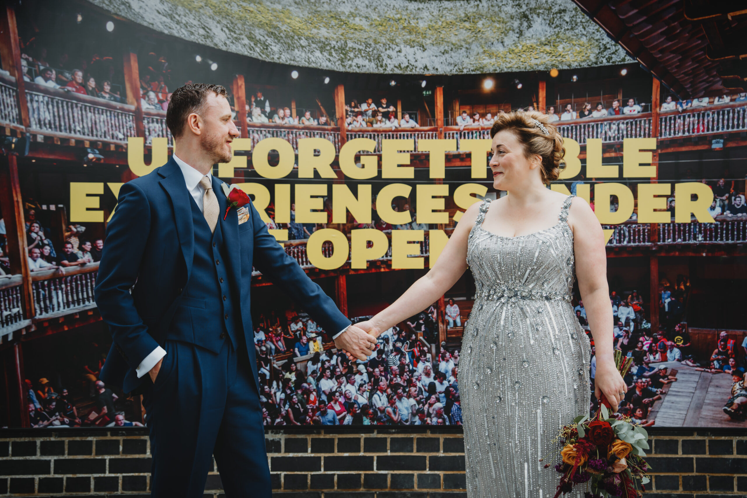 couple on their wedding day in London holding hands in front of a large theatre poster.