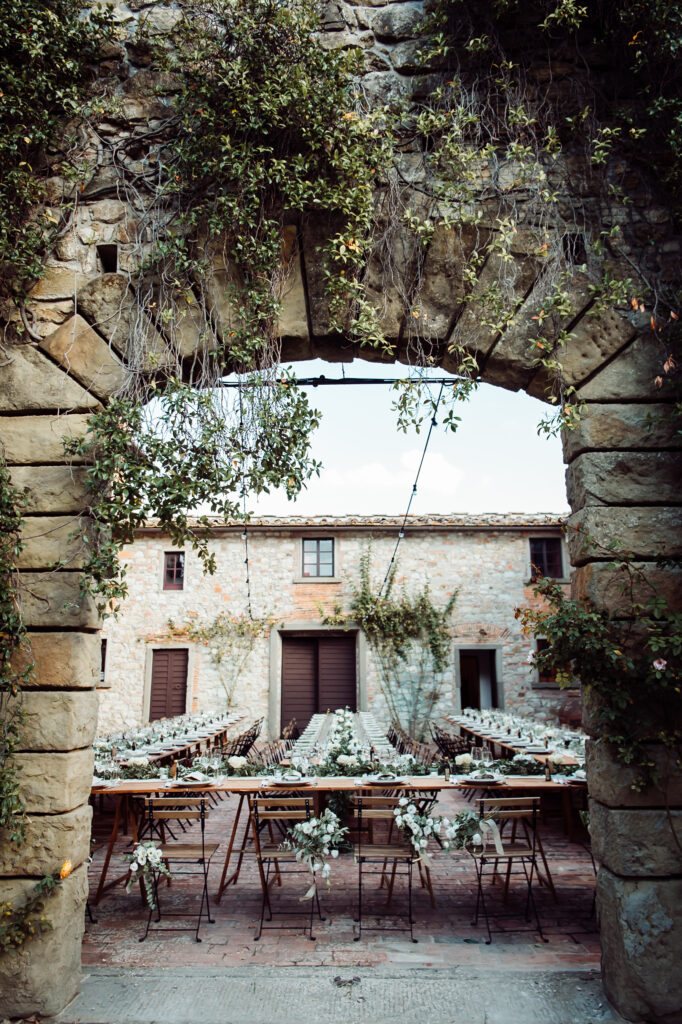 Elegant wedding reception tables decorated with white flowers in the stone courtyard of Castello di Cafaggio