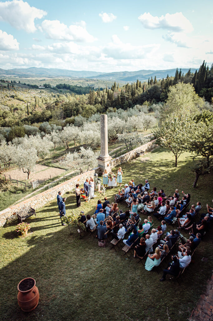 Aerial view of the wedding ceremony with guests and the surrounding Chianti countryside. Bride and groom exchanging vows under the Tuscan sky, captured by a Castello di Cafaggio Wedding Photographe