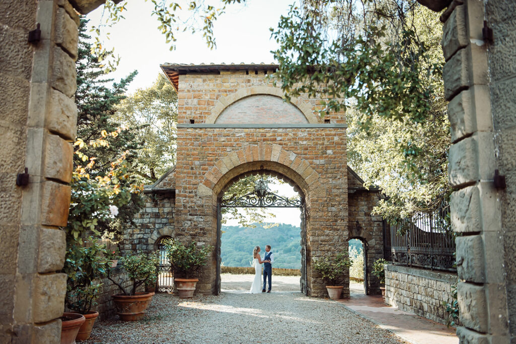 Bride and groom standing in a grand castle archway, looking at each other 