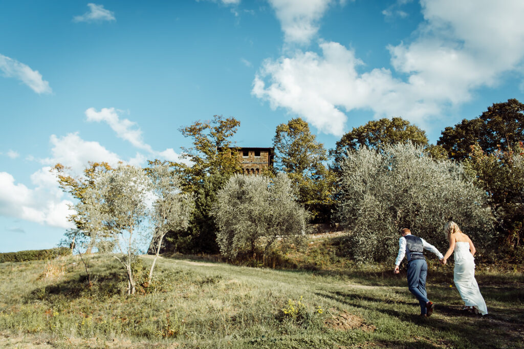 Bride and groom walking up a hill with the castle hidden among the trees during their Tuscan wedding