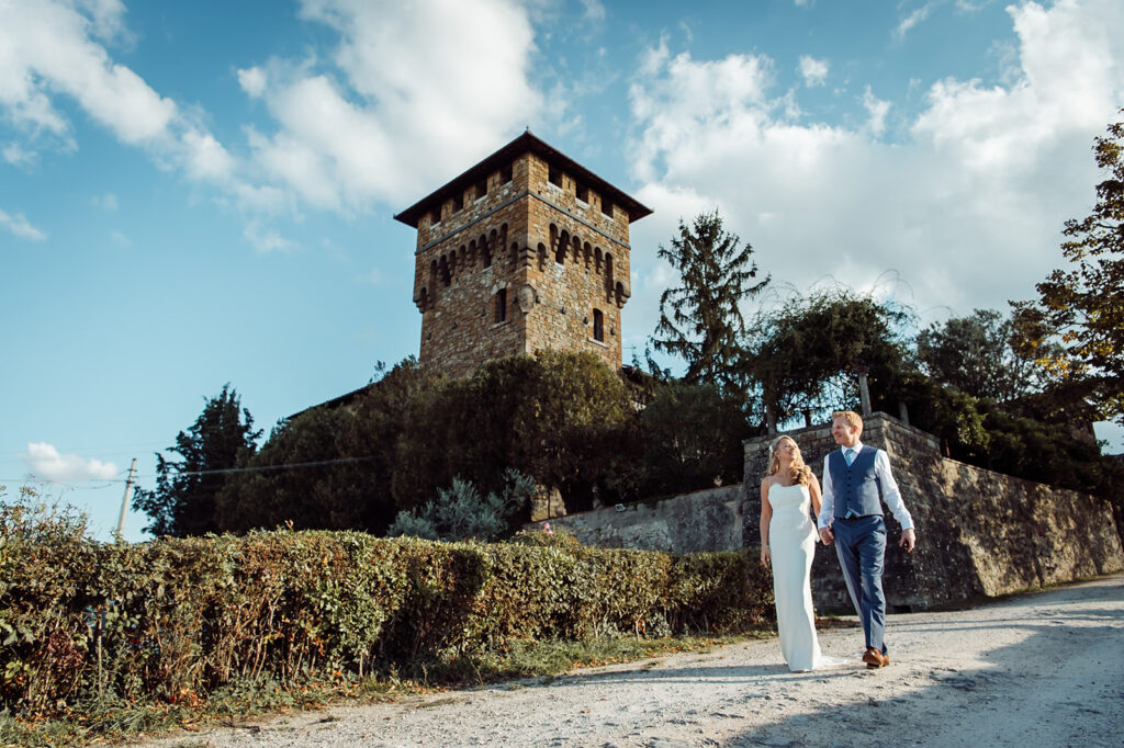 Bride and groom holding hands walking down a paved hill with the castle in the background.