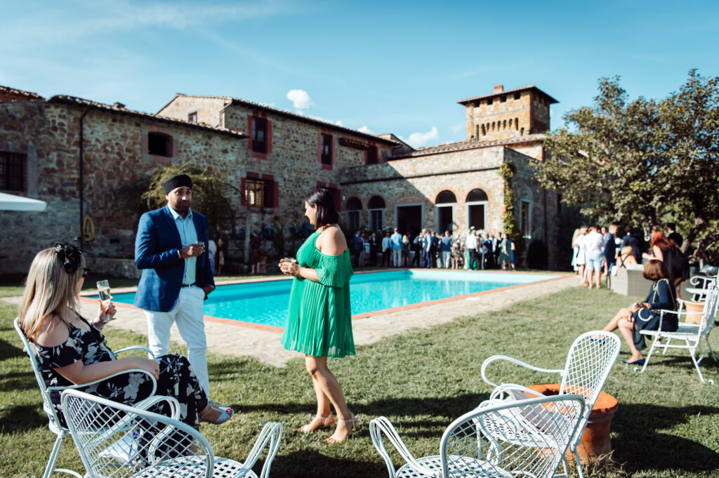 Wedding guests enjoying drinks and socialising by the pool outside Castello di Cafaggio.