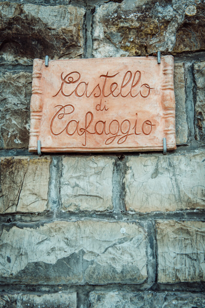 Hand-carved stone sign reading “Castello di Cafaggio” mounted on an old stone wall in Tuscany