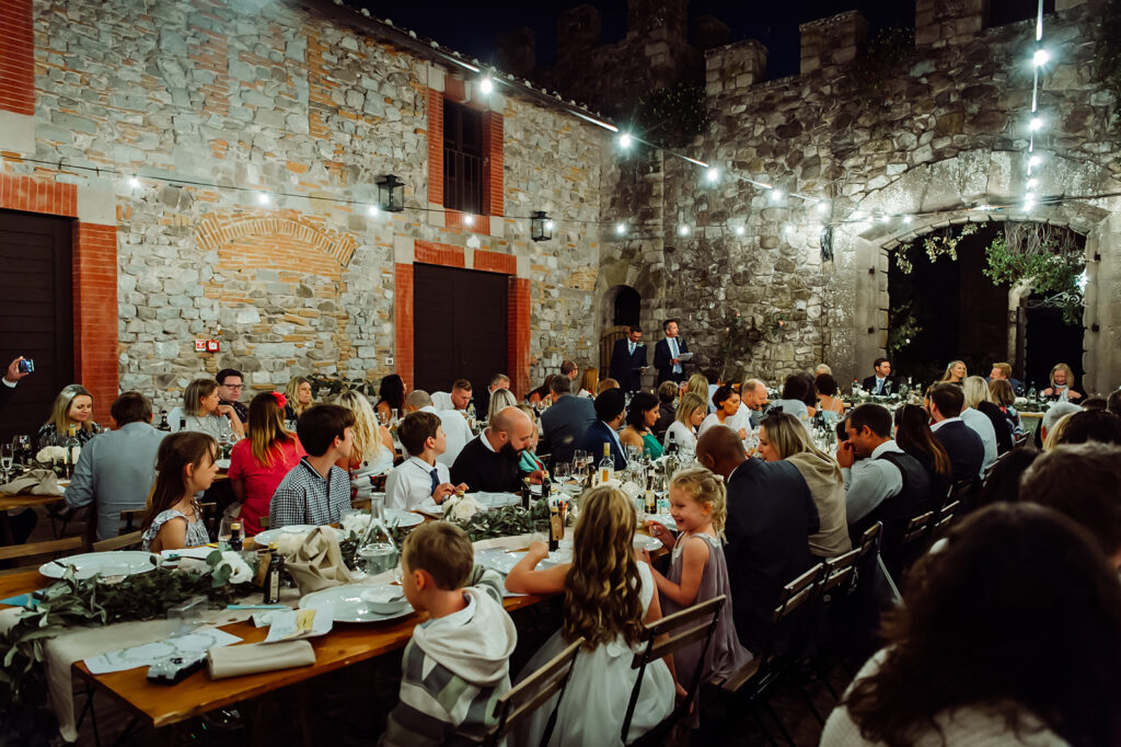 Wide shot of guests seated at long tables under twinkling lights during a Tuscan wedding dinner